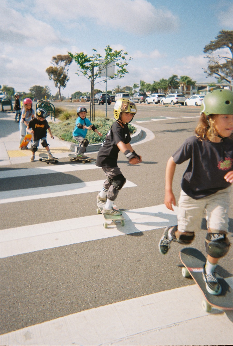 Kids on skateboards crossing a street in Encinitas on a sunny afternoon.