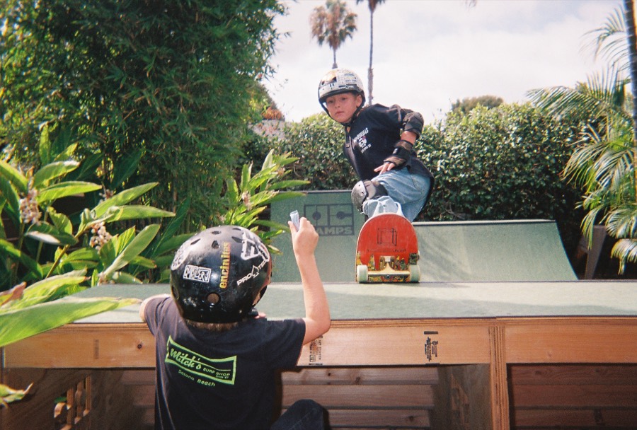 A young skater dropping in on a backyard ramp while a friend watches.