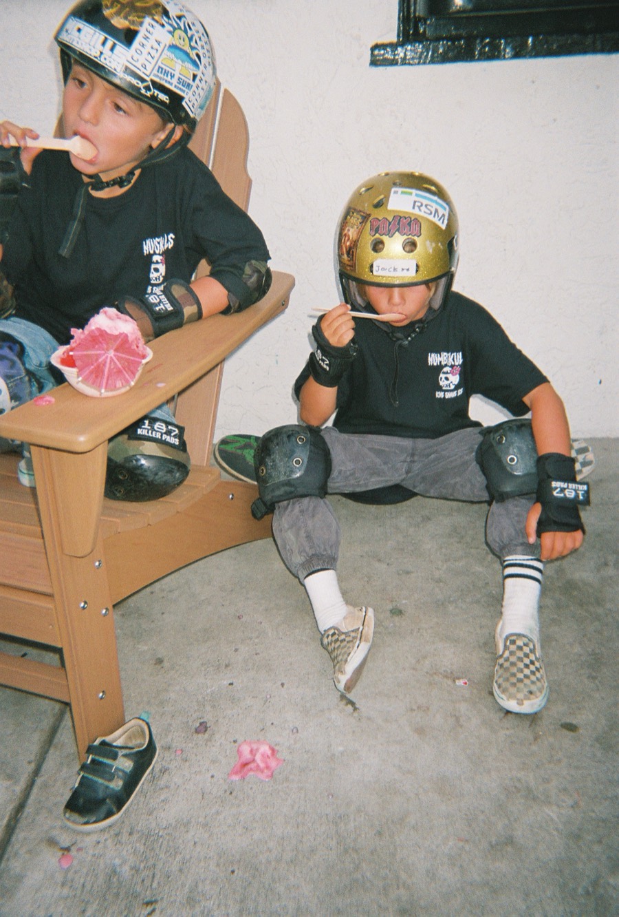 Two helmeted skaters taking a break with shave ice.